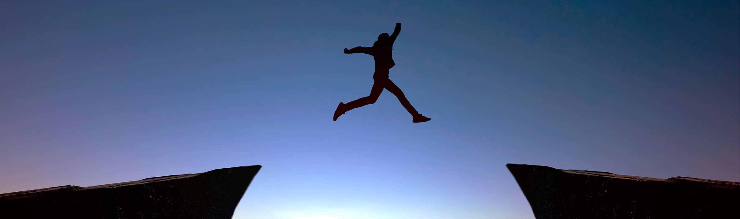 man jumping from one cliff to another