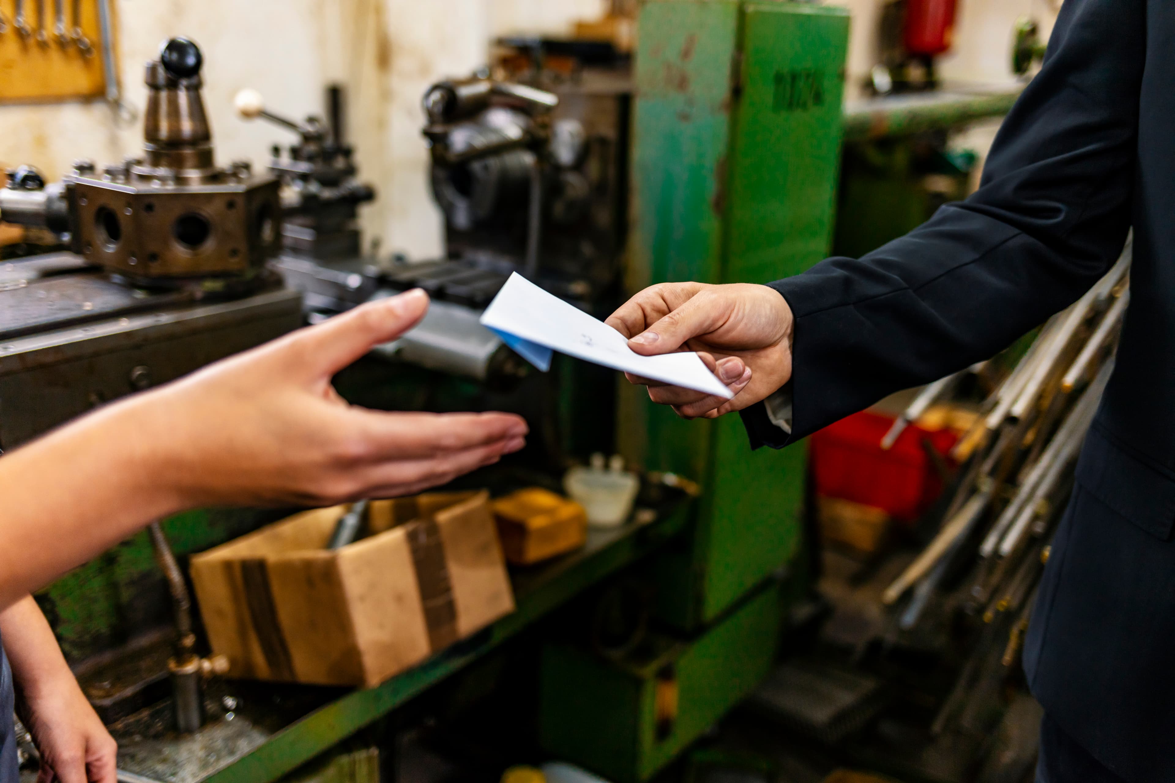 Human hand handing over a paper sheet to the other human hand in garage or factory type of environment.