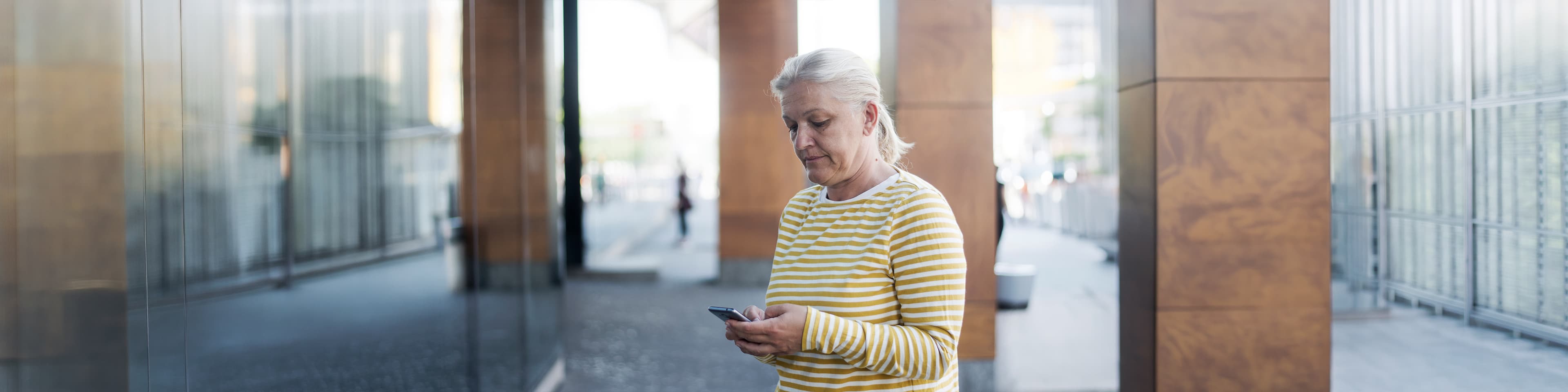 middle age white woman standing outside officess building and emailing someone with her smartphone
